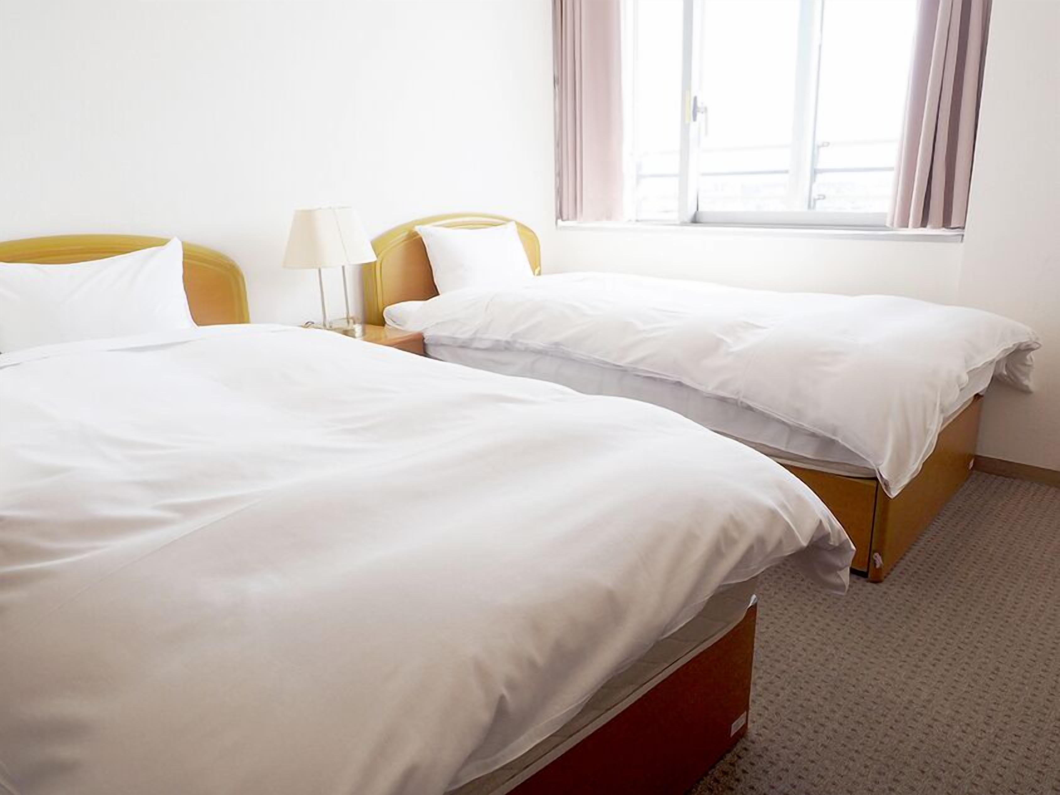 Una habitación de hotel con dos camas, una ventana con cortinas y una lámpara en la mesita de noche.