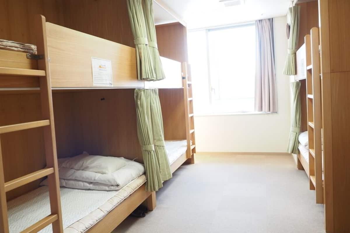 Une chambre avec un lit superposé, une fenêtre, des rideaux et une armoire en bois.