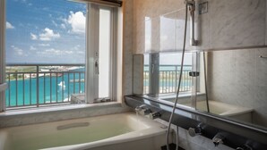Une salle de bain équipée d’une baignoire, d’une douche et d’une grande fenêtre donnant sur la mer.