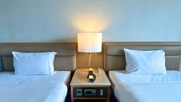 A hotel room with two beds, a nightstand with a lamp, and a control panel.
