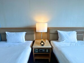 Habitación de hotel con dos camas, una mesita de noche con una lámpara y un panel de control.