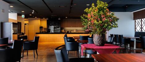 Un restaurante moderno con zona de comedor de madera, sillas negras y una mesa central con mantel rojo.