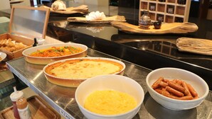 Une table de buffet proposant divers plats, notamment une tarte, un bol de maïs et un bol de saucisses.