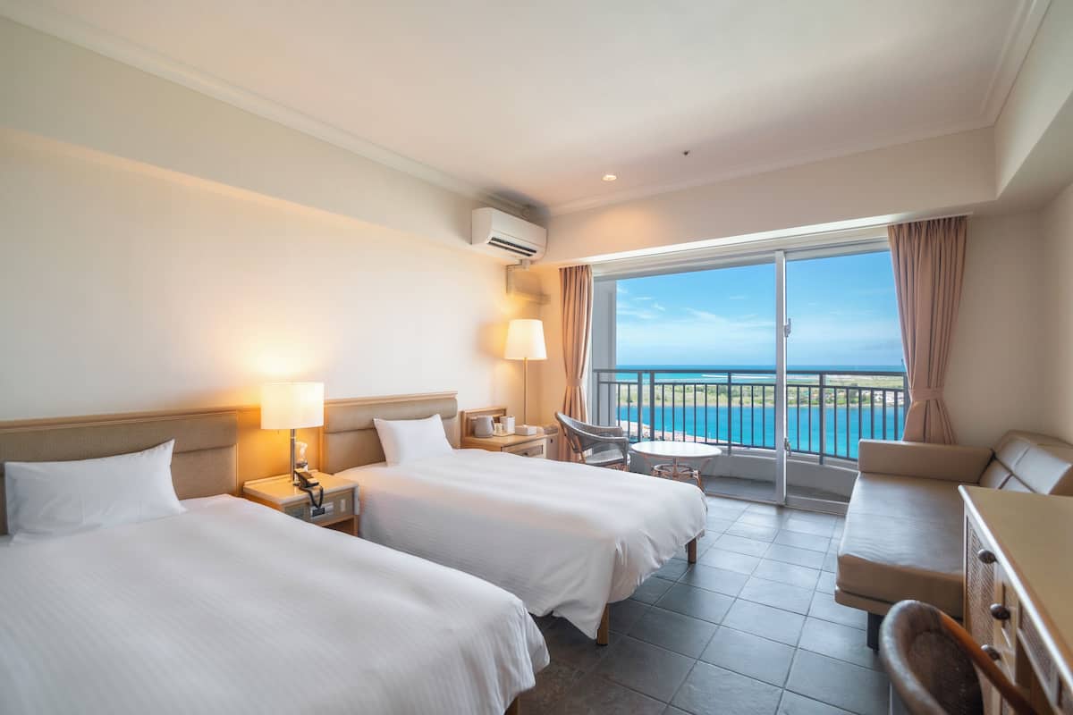 Hotelkamer met twee bedden, een balkon met uitzicht op zee, een tafeltje en een bank.