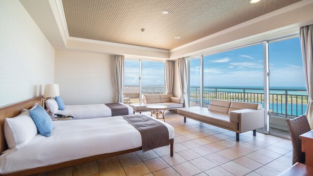 Une chambre d’hôtel avec deux lits, un balcon avec vue et un coin salon.