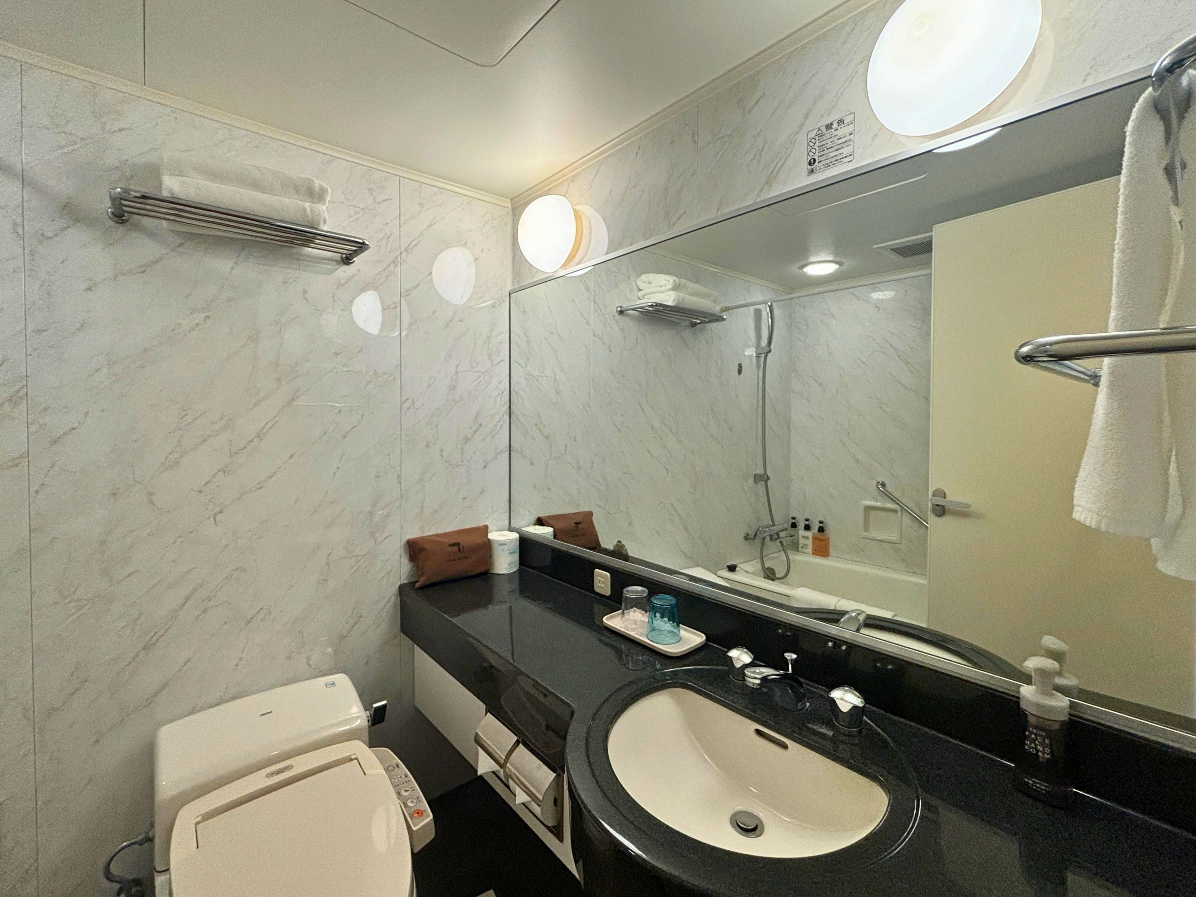 A modern bathroom with a marble wall, a black sink, a toilet, and a large mirror.