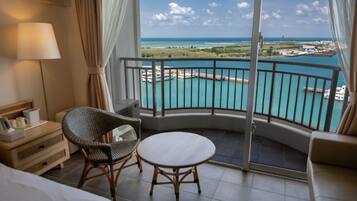 A hotel room with a balcony, a bed, a chair, a table, and a lamp.