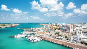 Un port de plaisance situé sur la côte, avec de nombreux bateaux amarrés, une jetée s’avançant dans l’eau et un paysage urbain avec des bâtiments en arrière-plan.
