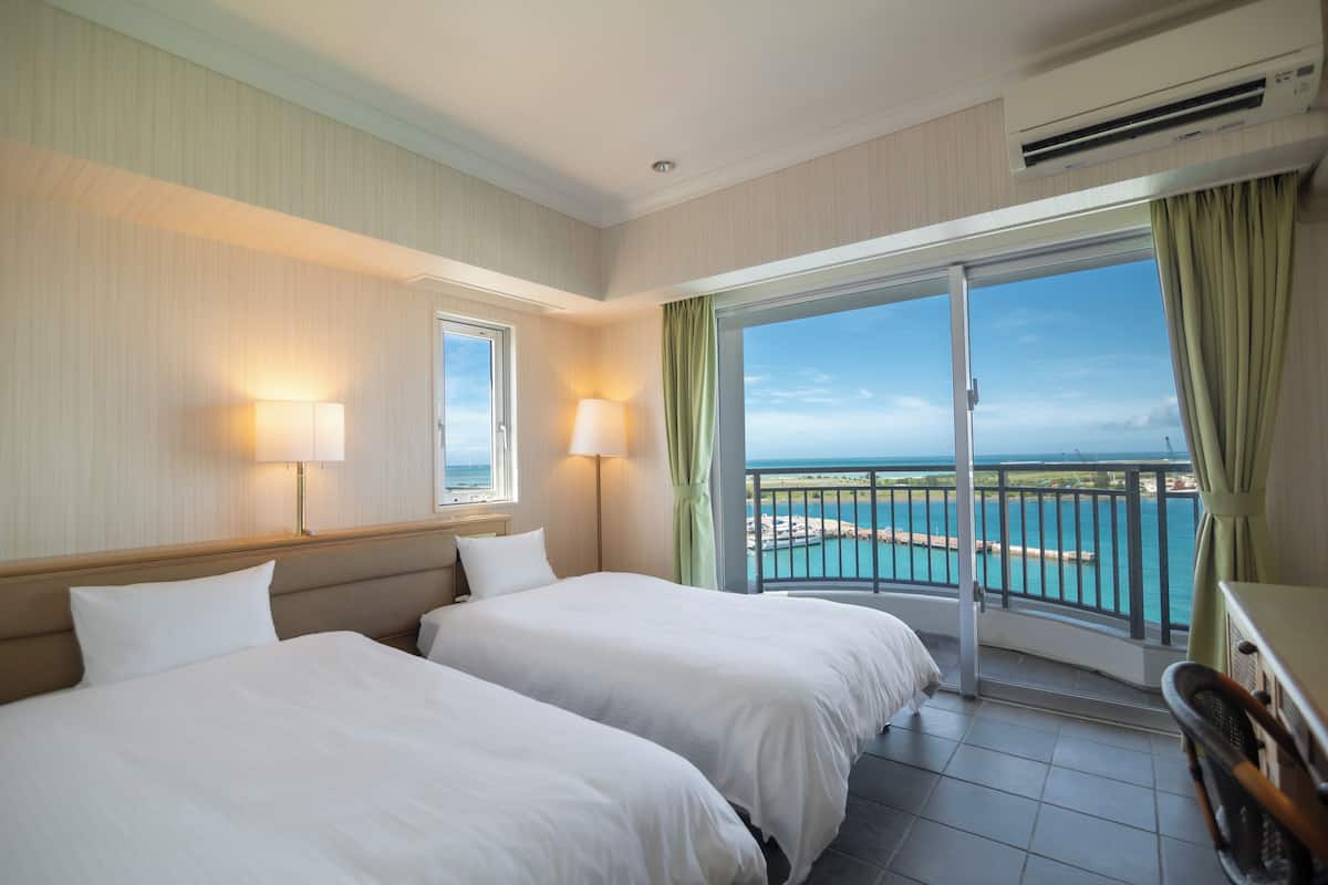 Een hotelkamer met twee bedden, een balkon met uitzicht op zee en een airconditioning.