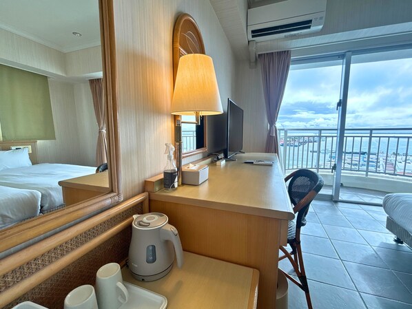 A hotel room with a bed, a desk with a lamp, a television, a coffee maker, and a view of the city through the window. - Hotel East China Sea (Ishigaki)