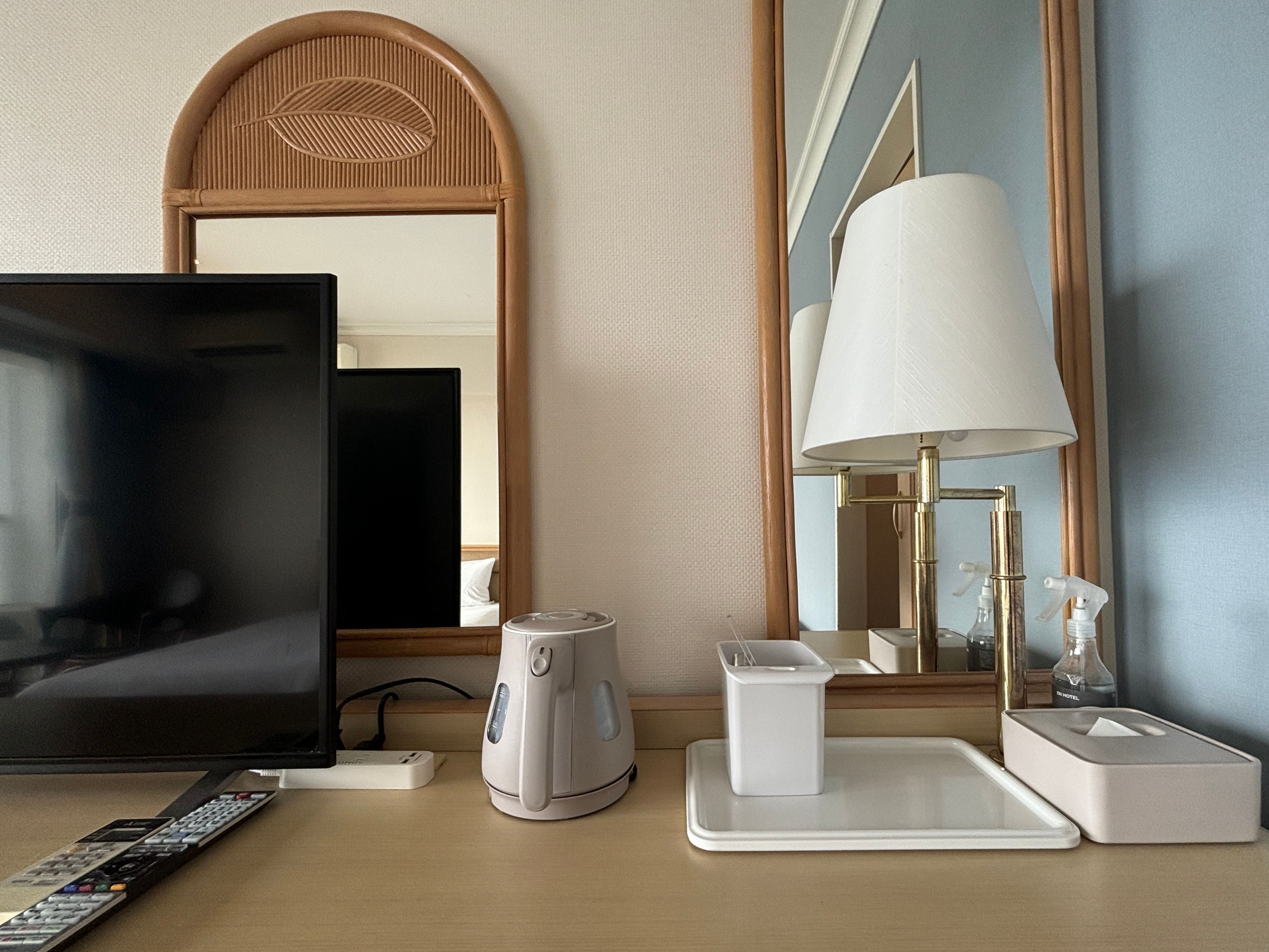 A hotel room with a television, a coffee maker, a remote control, a lamp, and a mirror.