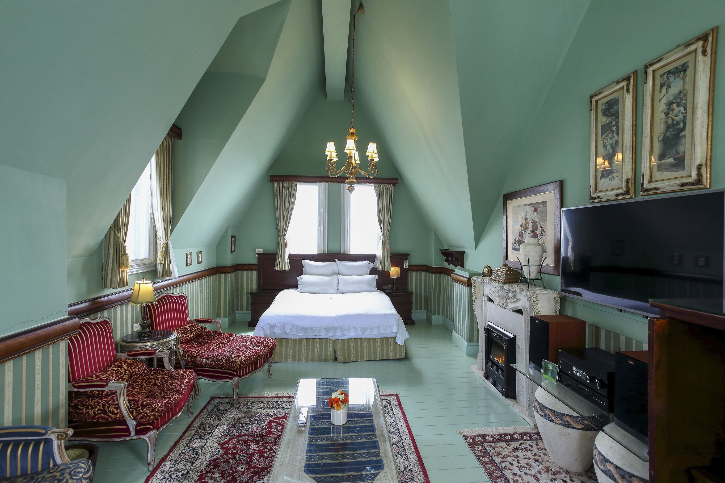 A bedroom with a large bed, a TV, a fireplace, and a chandelier.