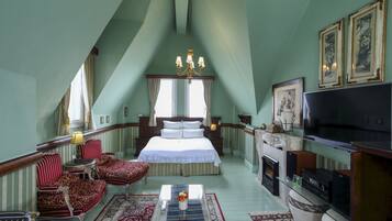 A bedroom with a large bed, a TV, a fireplace, and a chandelier.