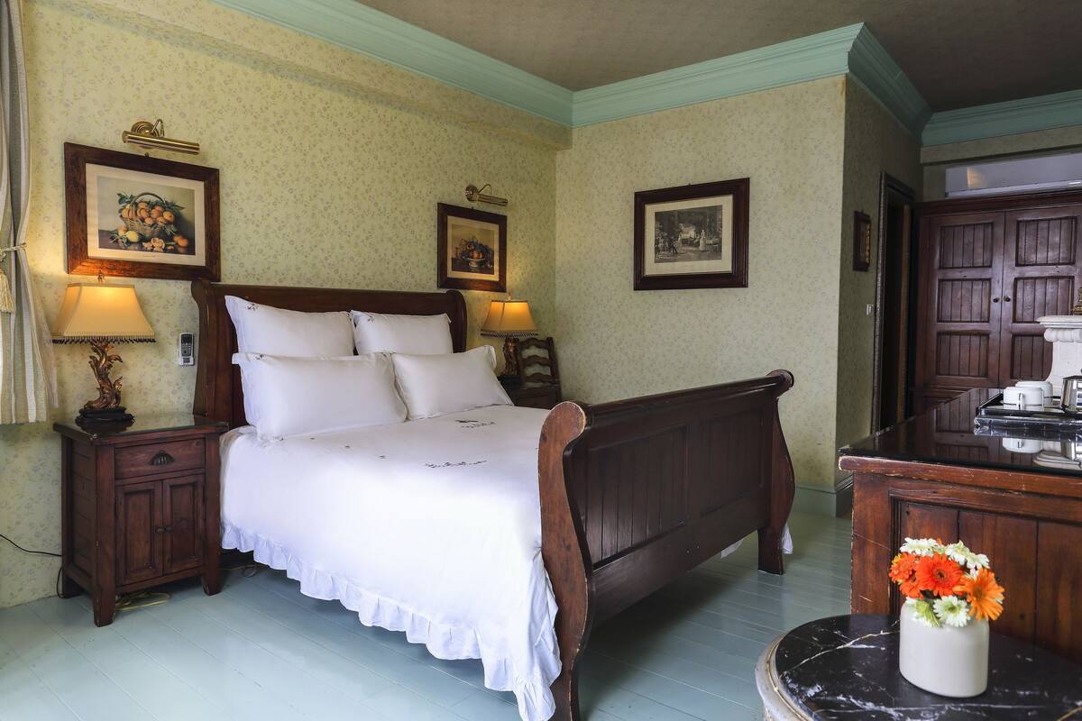 Une chambre à coucher avec un lit en bois, deux tables de chevet avec des lampes, une petite table et des tableaux encadrés accrochés aux murs.