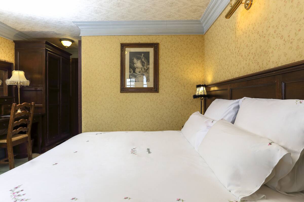Une chambre d’hôtel avec un grand lit, une table de chevet en bois, une chaise et un tableau encadré au mur.