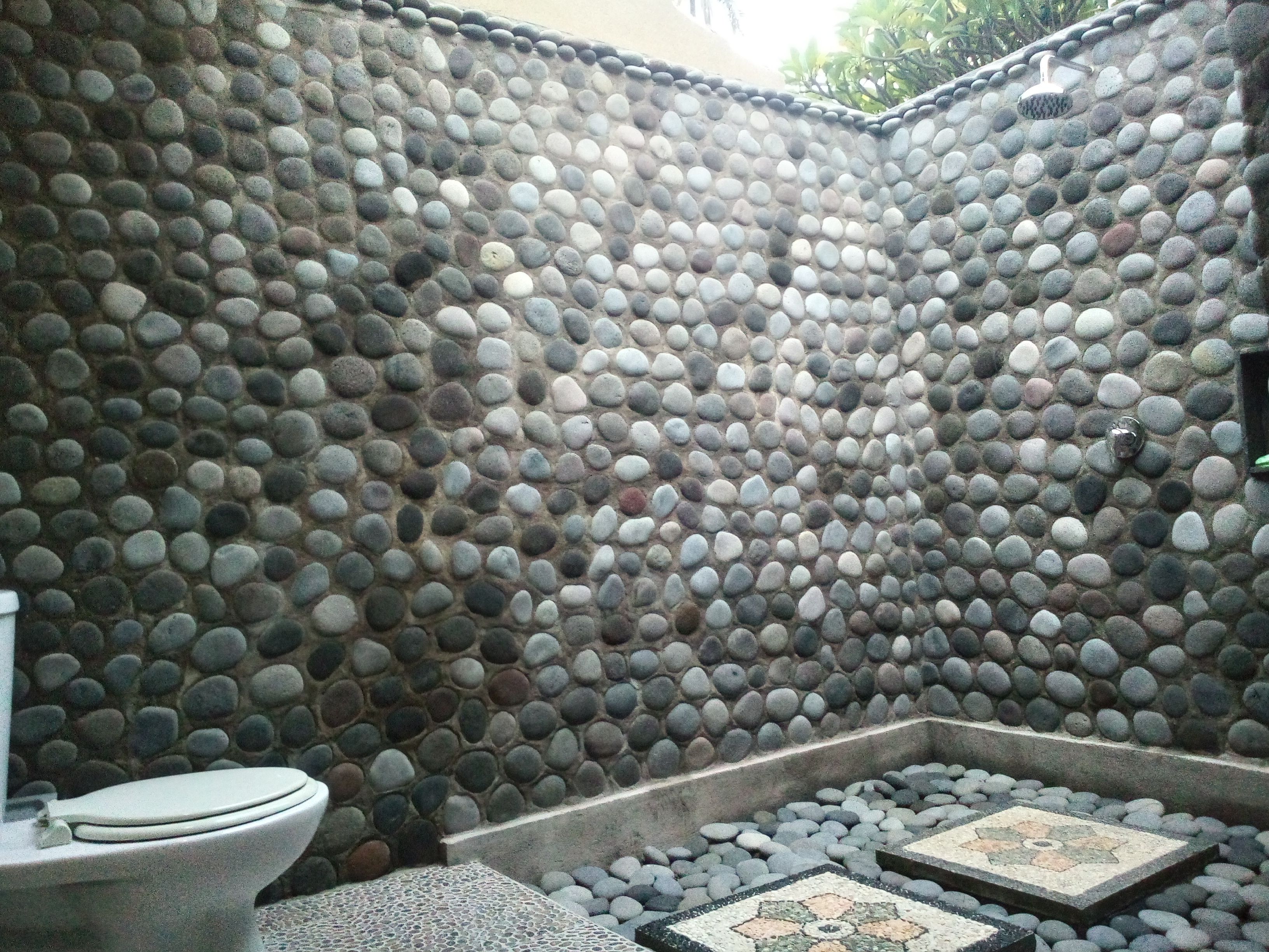 Un baño con pared de piedra, un inodoro y una pequeña zona con azulejos.