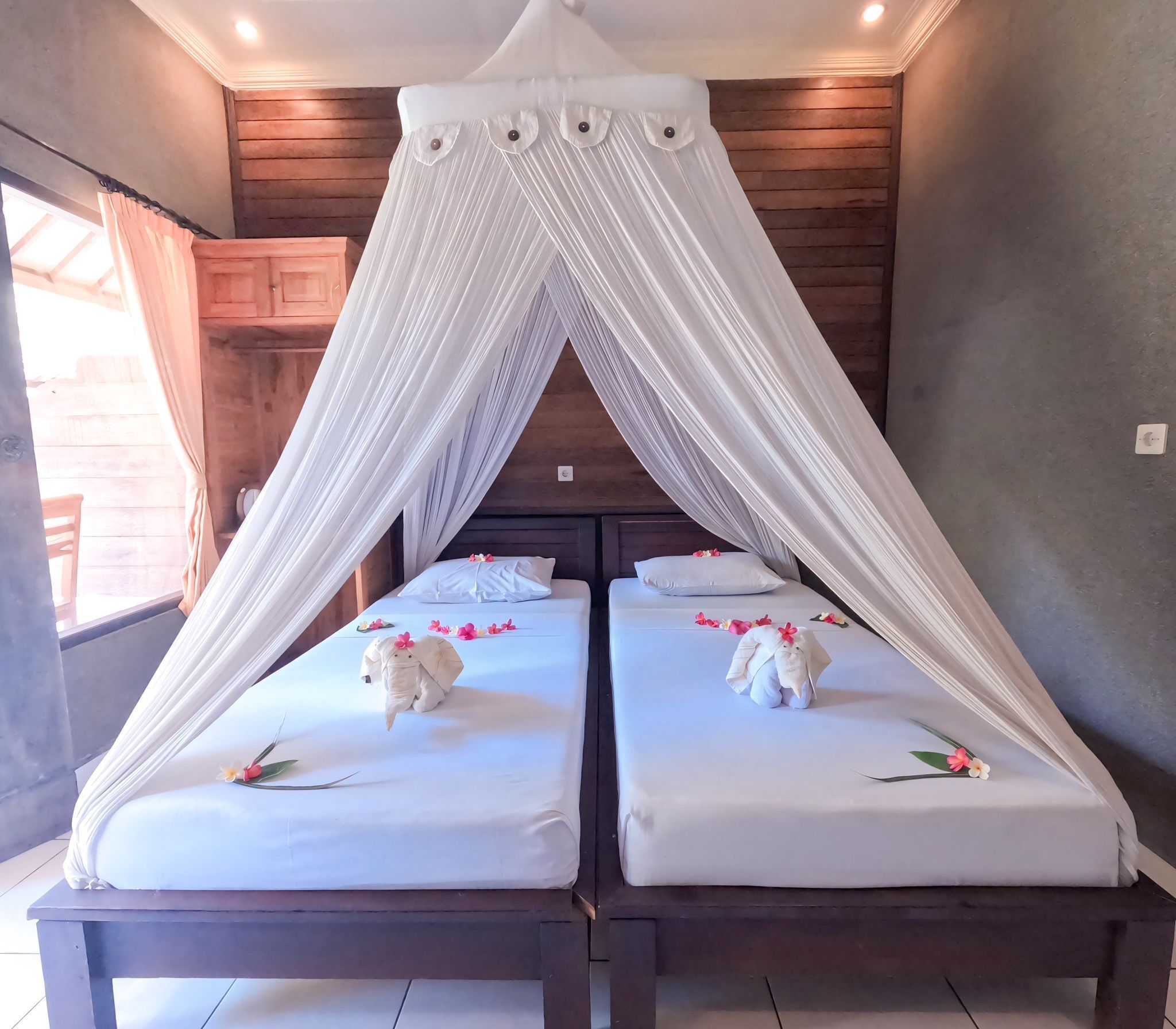 A room with a canopy bed, two pillows, and a small table with a flower.