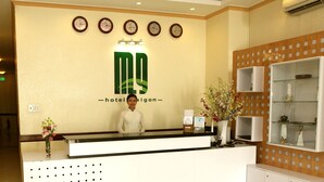A hotel reception desk with a logo, clocks, and a vase of flowers.