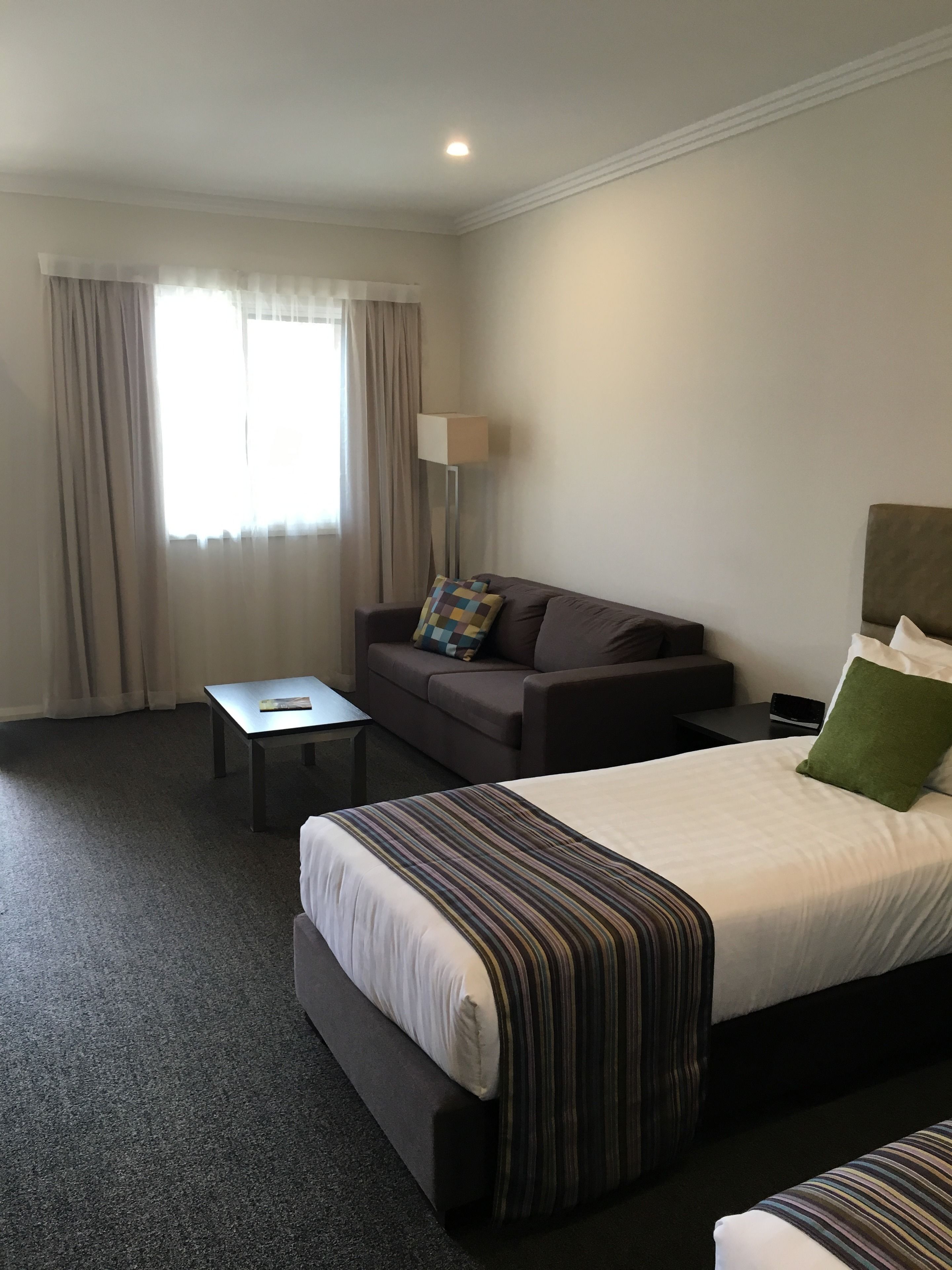 A hotel room with a bed, a sofa, a small table, a lamp, and a window with curtains.