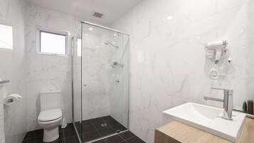 Ein modernes Badezimmer mit einer gläsernen Duschkabine, einem weißen Waschbecken mit Chromarmatur und einem an der Wand befestigten Föhn.