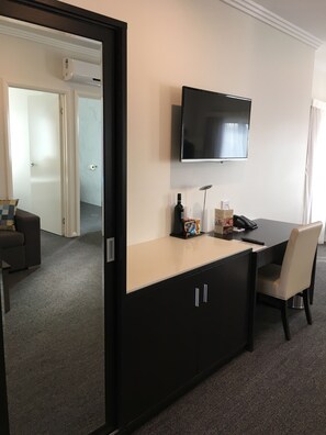 Une chambre d’hôtel avec un téléviseur fixé au mur, un bureau avec une chaise et une porte donnant sur une autre pièce.