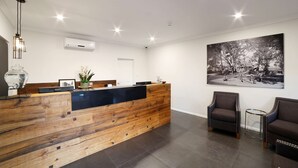 Un área de recepción con un mostrador de madera, una barra negra, una fotografía grande en blanco y negro en la pared, y dos sillones tapizados.