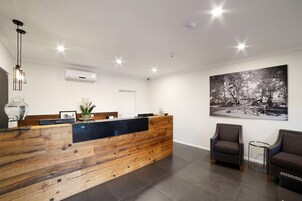 A reception area with a wooden reception desk, a black counter, a large black and white photograph on the wall, and two upholstered chairs.