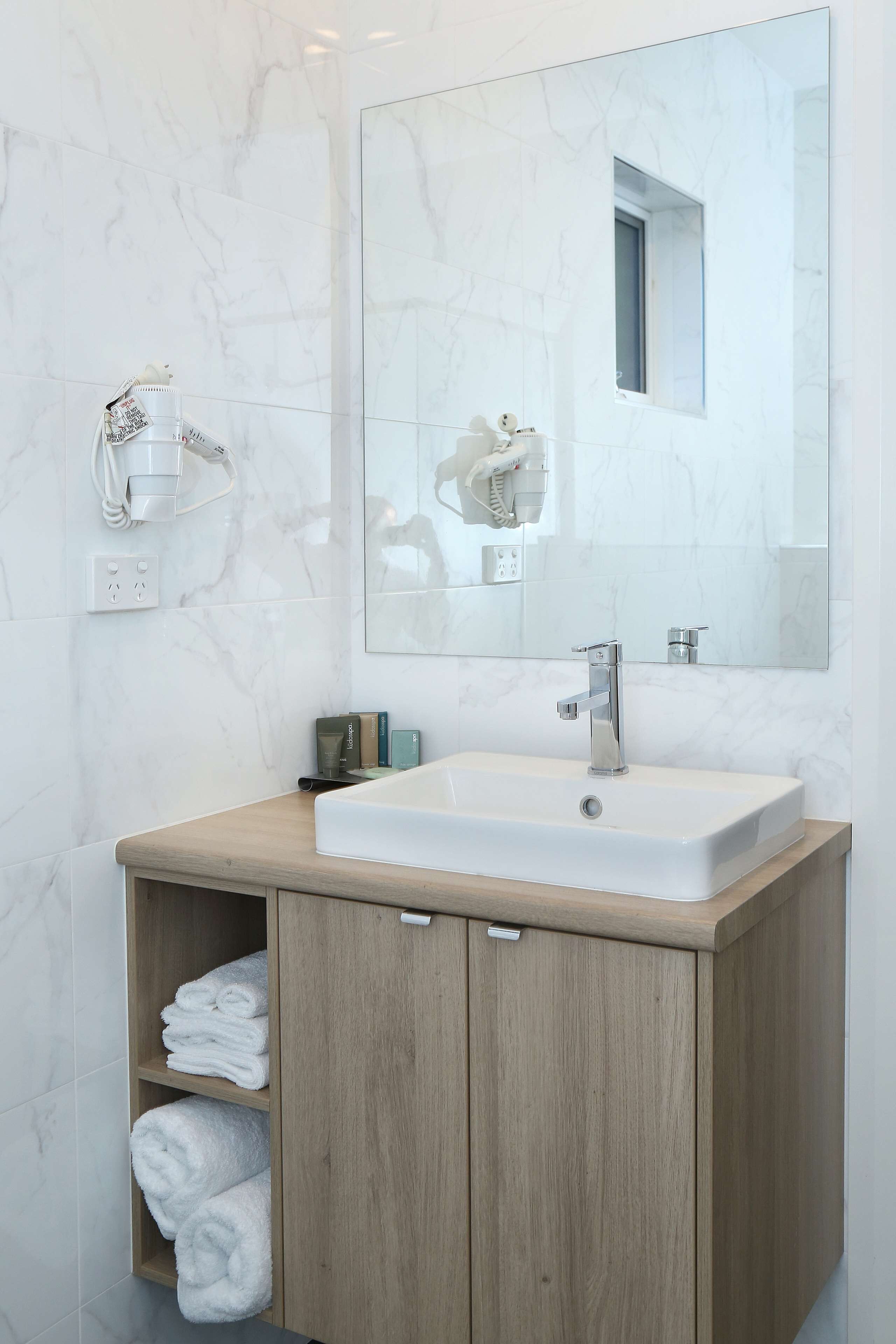 A bathroom with a white marble sink, wooden vanity, and a large mirror.