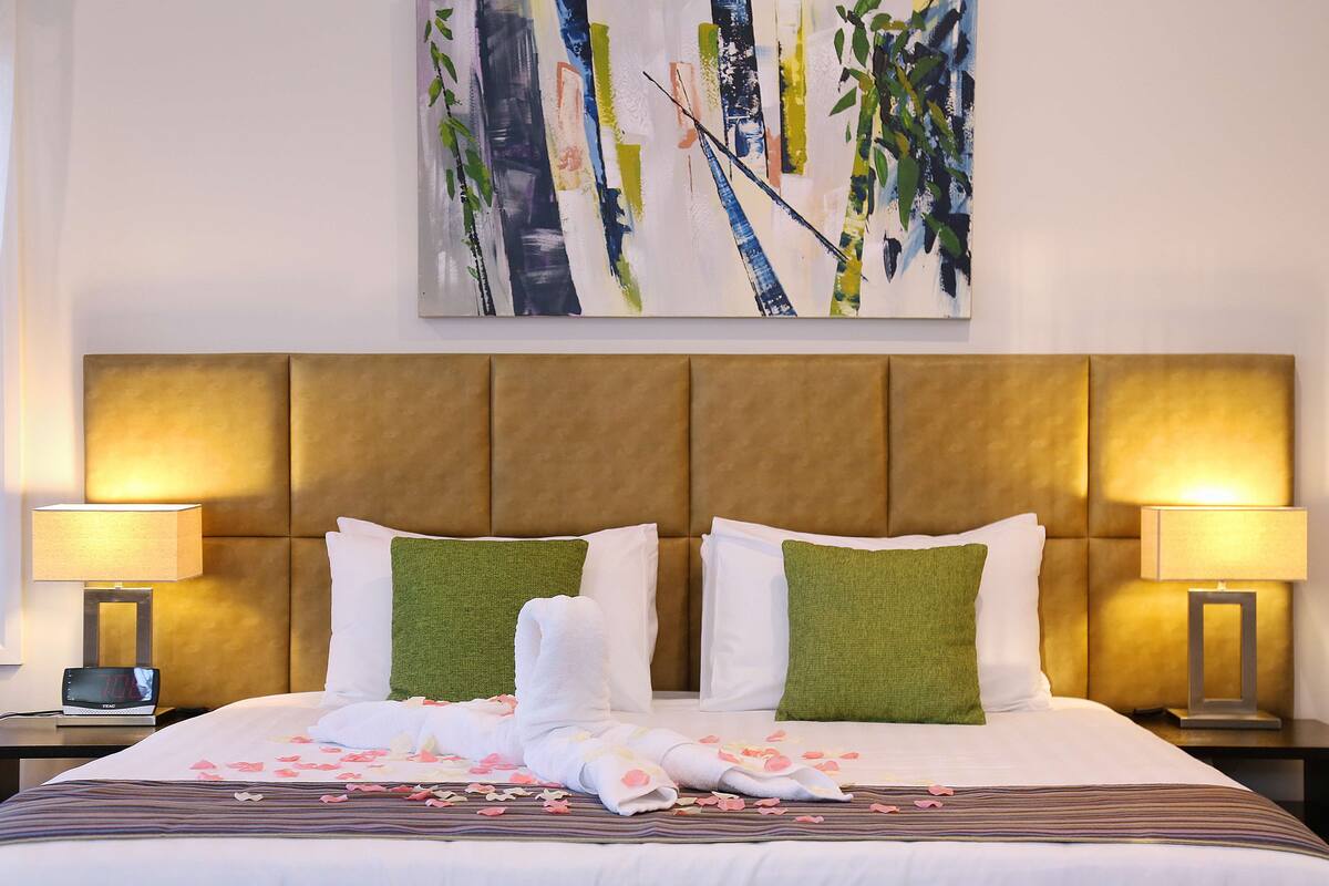 Una habitación de hotel con una cama grande, dos almohadas verdes, ropa de cama blanca y un cuadro en la pared.