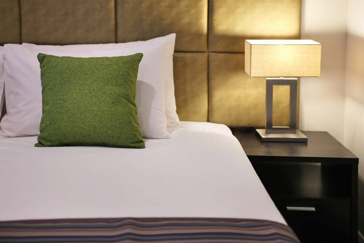 Una cama bien hecha con almohadas blancas y verdes, una manta a rayas y una mesita de noche con una lámpara.
