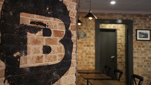 Un muro de ladrillo con un gran diseño similar a un grafiti oscuro. Se ven mesas y sillas al fondo, lo que sugiere un área de comedor.
