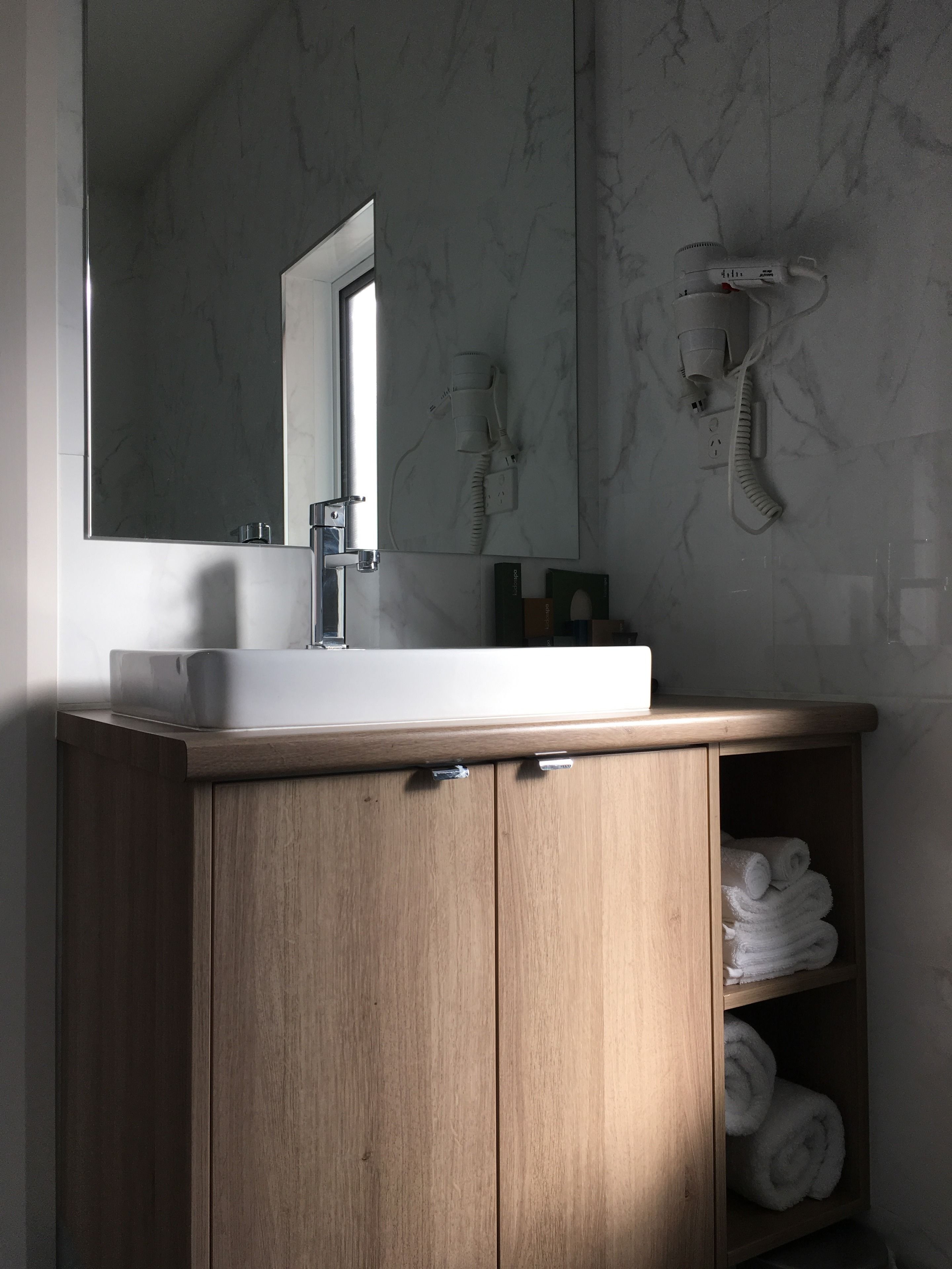 A bathroom with a wooden vanity, a white sink, a mirror, and a towel rack.