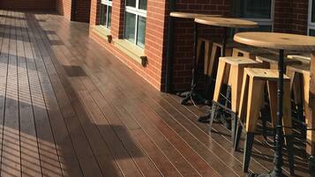 Un bâtiment en briques doté d’une terrasse en bois et d’un espace extérieur aménagé pour s’asseoir.