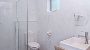 A modern bathroom with a glass shower enclosure, a toilet, a small window, and a sink with a mirror.