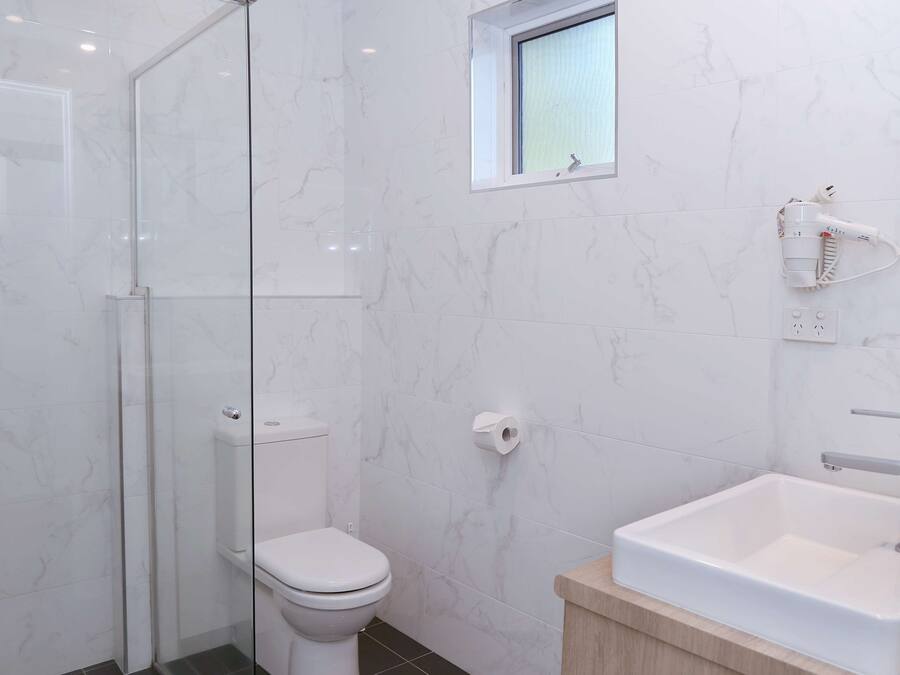 A modern bathroom with a glass shower enclosure, a toilet, a small window, and a sink with a mirror.