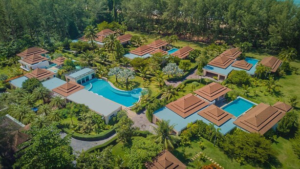 An aerial view of a resort with multiple bungalow-style buildings, a central swimming pool, and lush greenery surrounding the property.