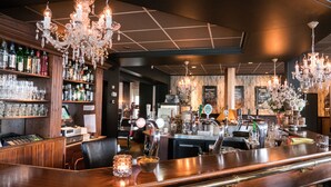 A bar area with wooden shelves stocked with bottles, a bar counter with a cash register, and a chandelier. - Hotel Café Restaurant Dallinga (Sluiskil)