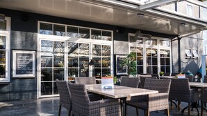 An outdoor cafe area with wicker furniture and a menu board. - Hotel Café Restaurant Dallinga (Sluiskil)