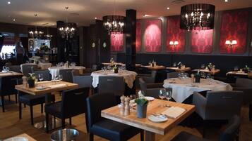 A restaurant with multiple tables, chairs, and chandeliers.