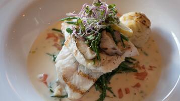 A plate of food with a piece of fish, greens, and a creamy sauce.