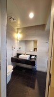 A modern bathroom with a white toilet, a black vanity with a white sink, a mirror above the sink, and a light fixture on the ceiling.
