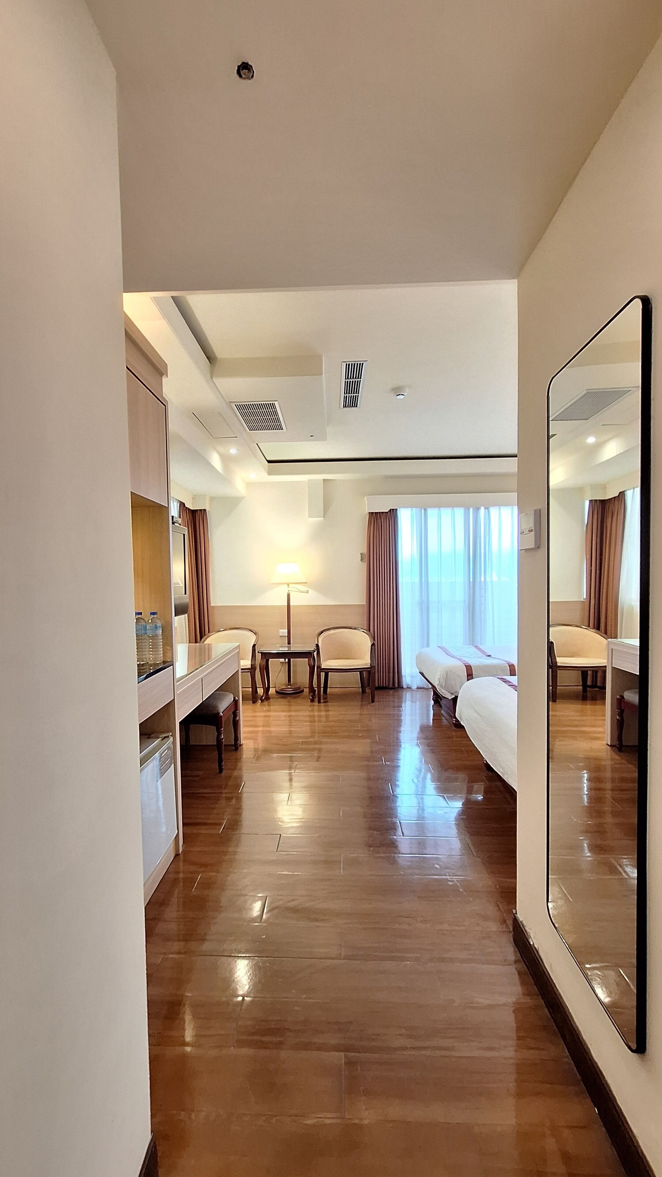 A hotel room with a bed, a desk, a chair, a mirror, and a window with curtains.