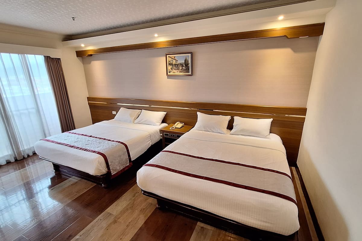 Habitación de hotel con dos camas, cabeceros de madera, un teléfono junto a la cama y un cuadro en la pared.
