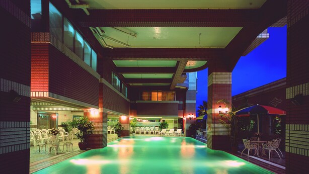 A swimming pool area with lounge chairs and tables, surrounded by brick walls and large windows. - Cheng Pao Hotel (Puli)