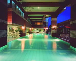 Un área de piscina con sillones de descanso y mesas, rodeada de muros de ladrillo y grandes ventanales.