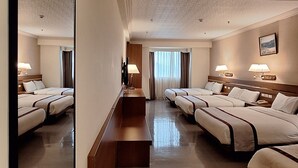 A hotel room with a large mirror, two beds, a wooden bench, a desk, and a window with curtains. - Cheng Pao Hotel (Puli)