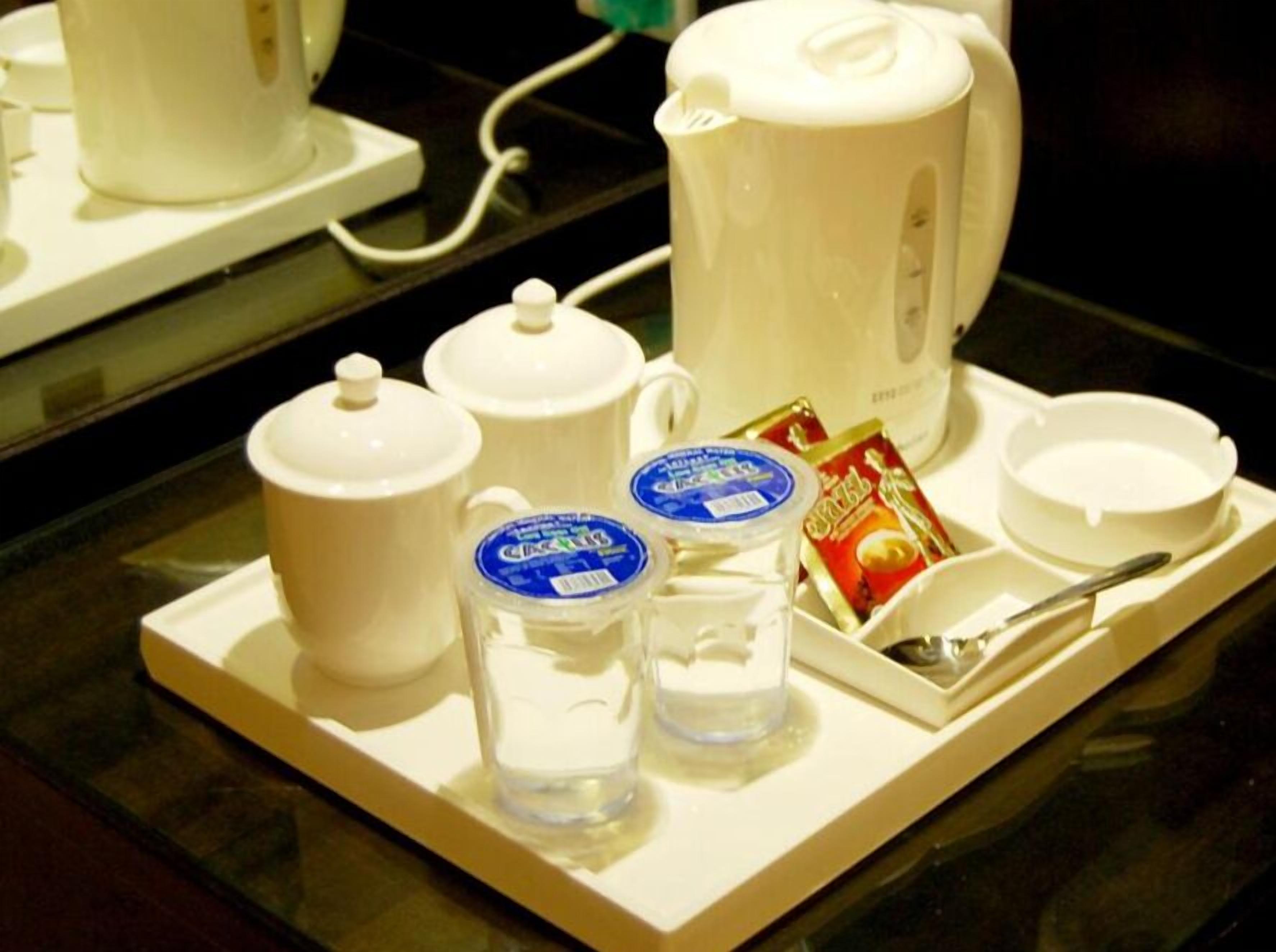 Una bandeja con cafetera, dos termos, un vaso de agua, un sobre de té, una cuchara y un bol.