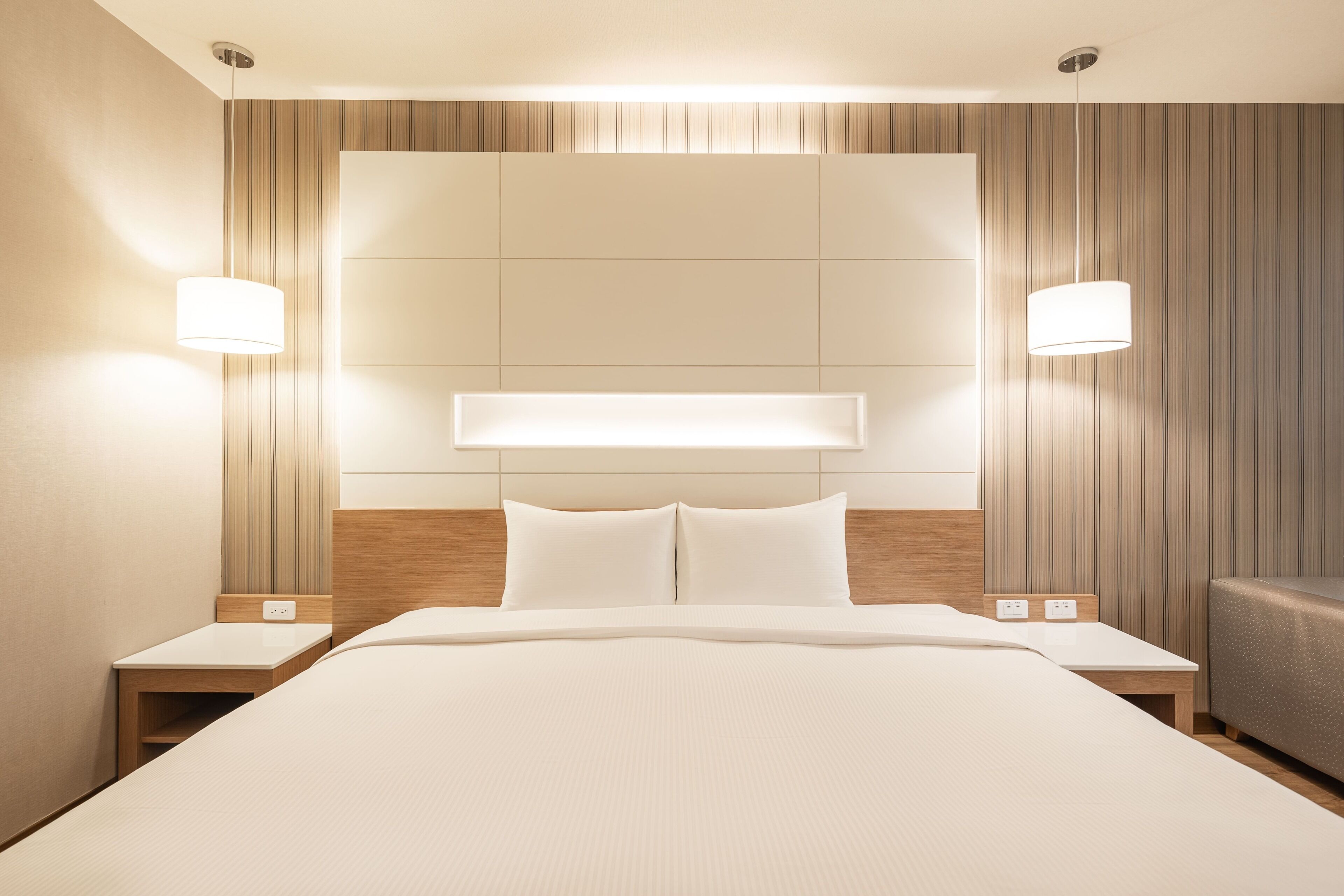 A modern hotel room with a large bed, two bedside tables, and a headboard with built-in lighting.