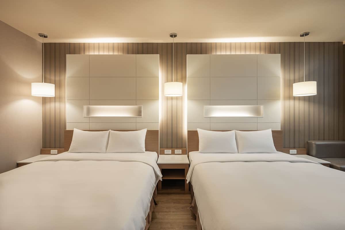 A hotel room with two beds, a wooden headboard, bedside lamps, and a nightstand.