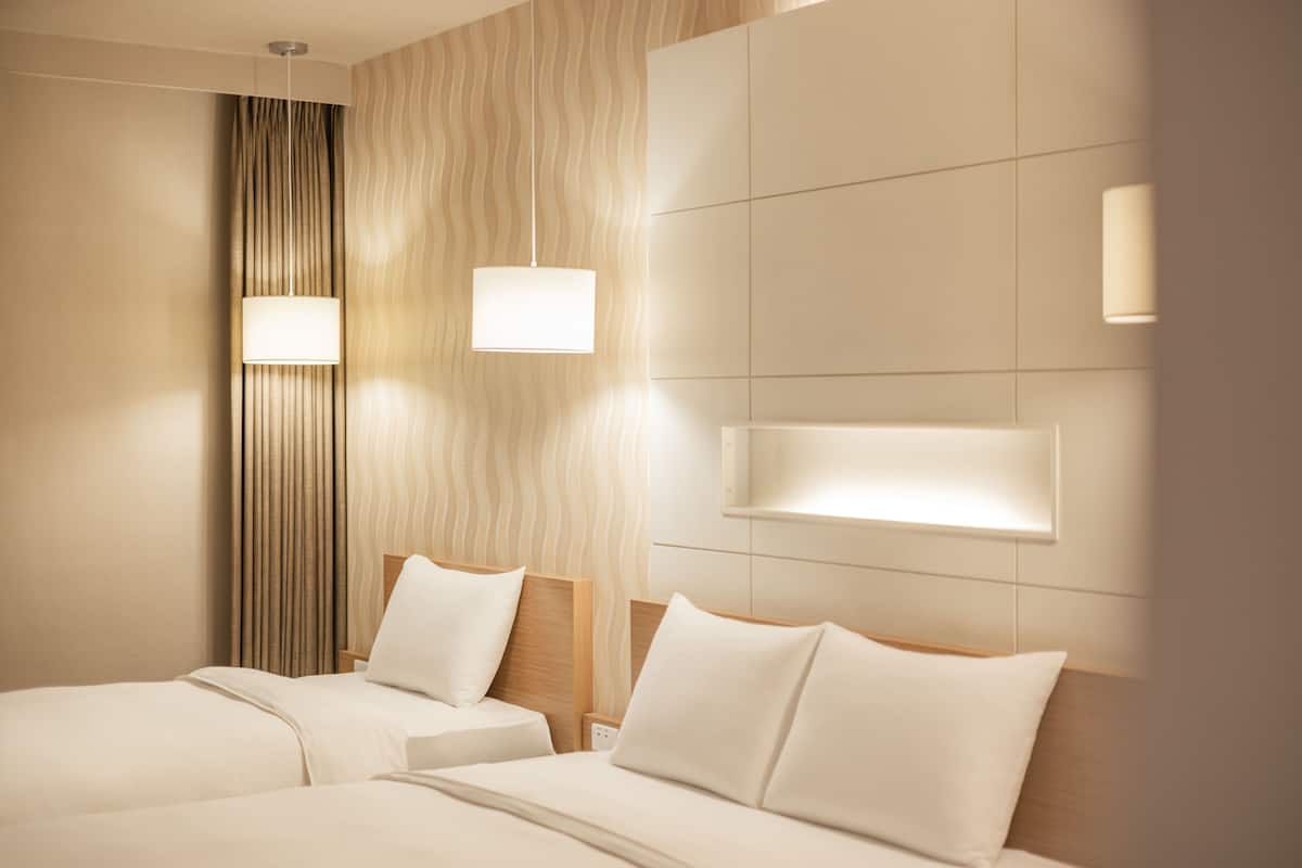 A hotel room with two beds, a large window, and a wall-mounted light fixture.